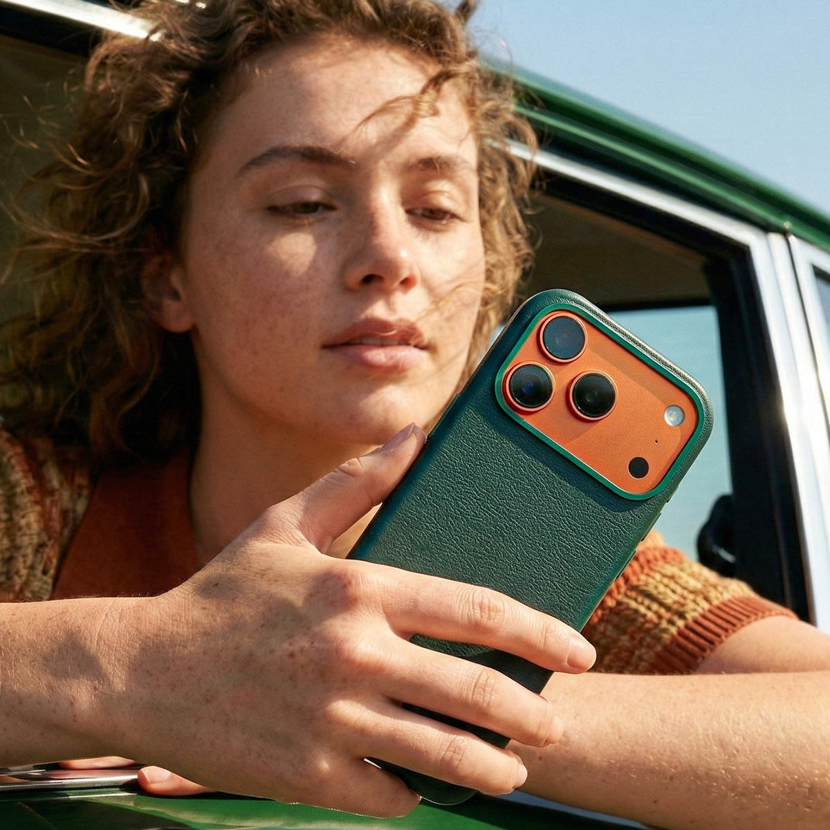Person holding a iphone 17 pro leather case in front of a vehicle racing green