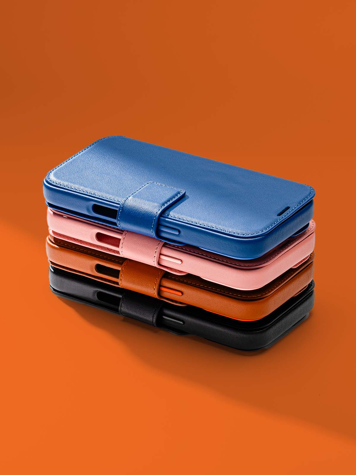 Stack of four leather wallet cases in blue, pink, brown, and black, on an orange background