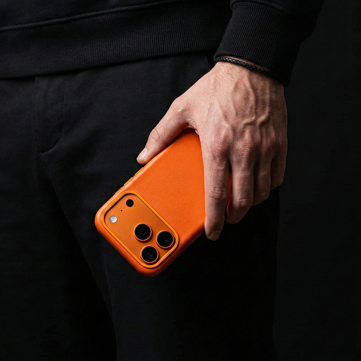 Hand holding an orange iphone 17 pro max leather case against a black background